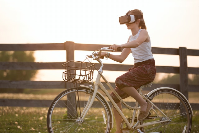Mulher andando de bicicleta enquanto mantém óculos de realidade virtual sugerindo que um dos benefícios do minimalismo digital é se manter na realidade.